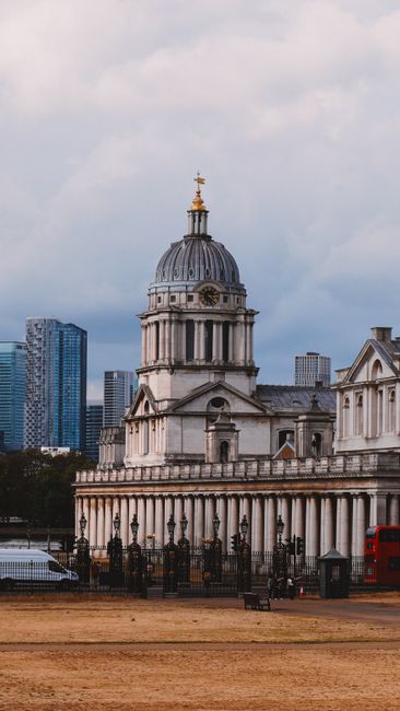 A historic domed building with classical architectural features, including columns and decorative stonework, situated in an urban environment with modern skyscrapers visible in the background. The clo